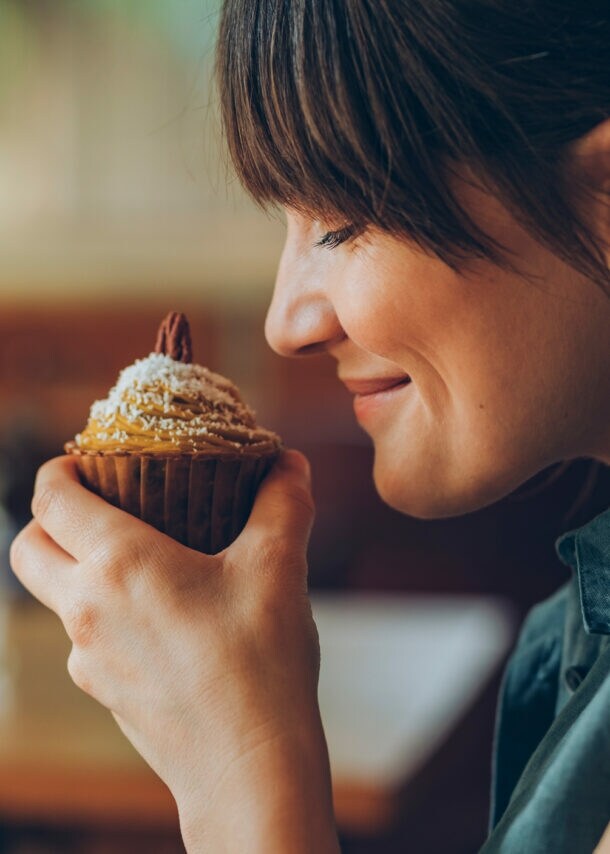 Eine Frau hält sich einen Nuss-Muffin an die Nase und lächelt, ihre Augen sind geschlossen.