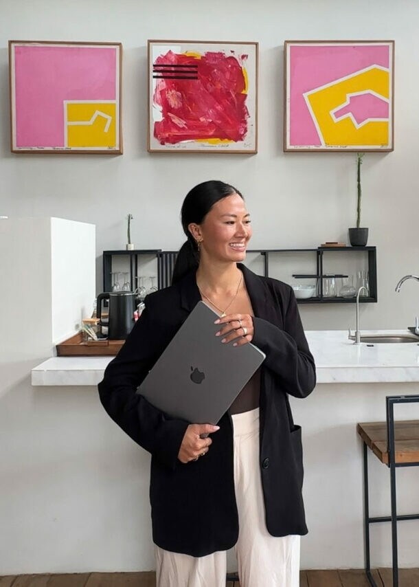 Eine lächelnde Frau mit Laptop unter dem Arm steht vor einer modernen Küchenzeile mit abstrakten Gemälden in einem Loft.