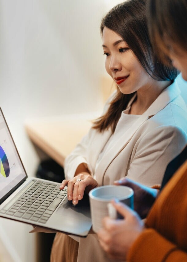Zwei Frauen schauen gemeinsam auf einen Laptop, dessen Bildschirm ein Tortendiagramm zeigt.
