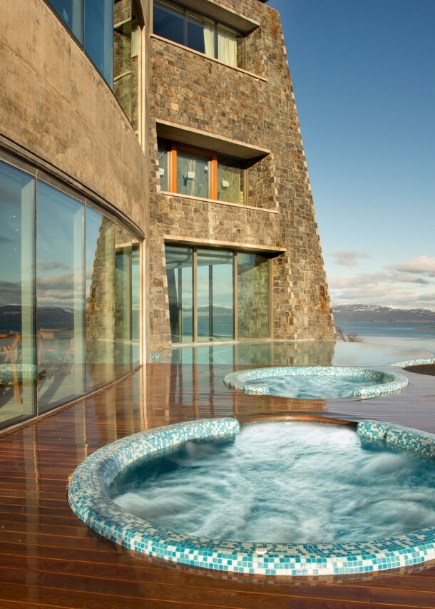 Jacuzzis auf einer Hotelterrasse mit Blick auf eine Schneelandschaft am Wasser.
