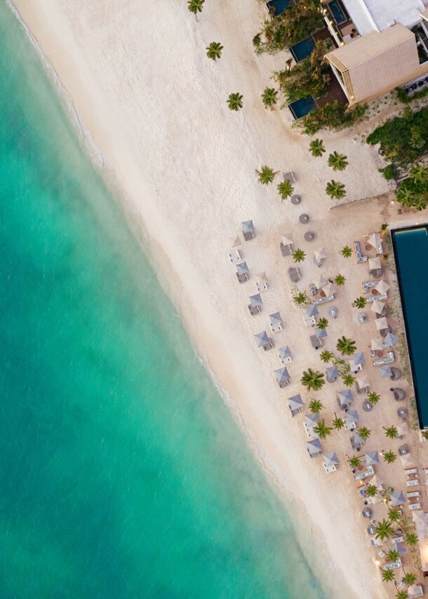 Hotelresort mit Pool und Sanstrand am türkisblauen Meer aus der Vogelperspektive.