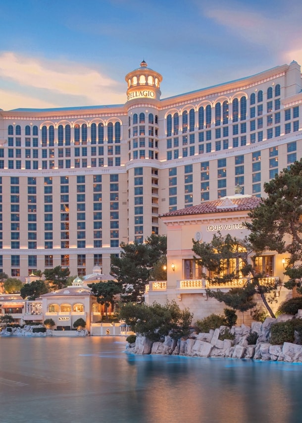Prunkvoller Hotelkomplex hinter einem künstlichem See mit beleuchteter Wasserfontäne bei Sonnenuntergang.