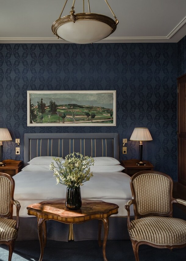 Gemütliches Hotelzimmer mit Doppelbett vor dunkelblauer Tapete und großem Holzkleiderschrank.