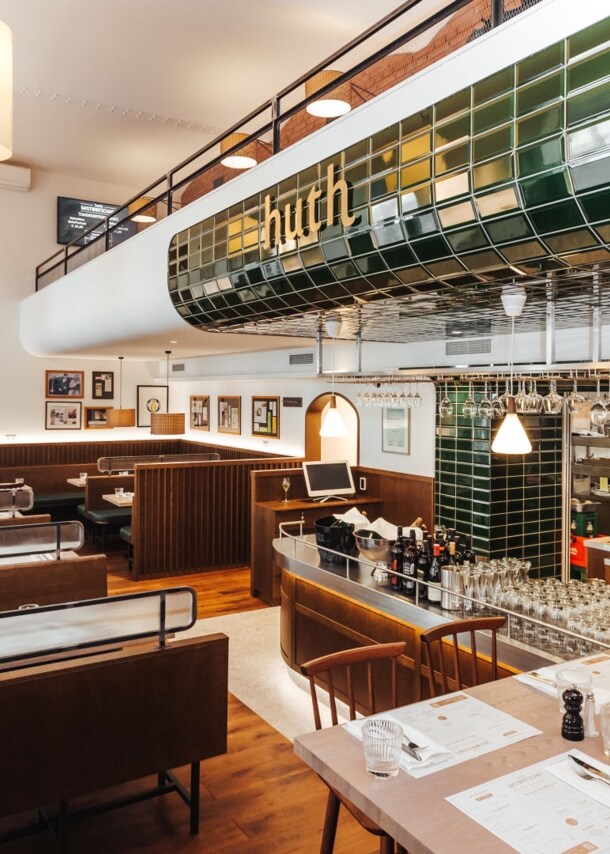 Moderner Speiseraum mit Holzmobiliar und Barbereich mit grünen Kacheln mit der Aufschrift huth.