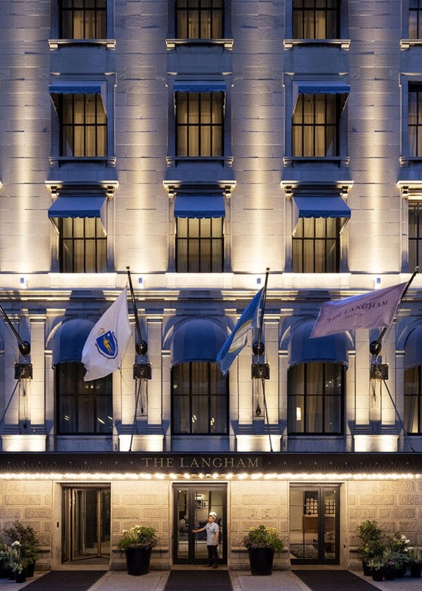 Beleuchtete Fassade eines Luxushotels mit wehenden Fahnen über dem Eingangsbereich.