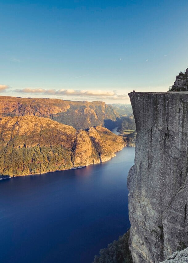 Fjordlandschaft an einem klaren Tag mit Personen auf einer beeindruckenden Felsklippe.