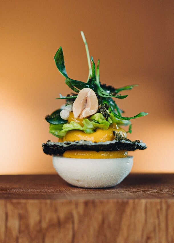 Eine exklusive Vorspeise aus geschichteten Zutaten, angerichtet auf einem Holzsockel vor unscharfen Hintergrund.
