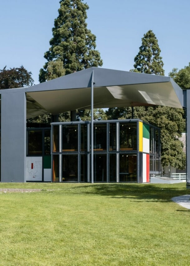 Eine Familie läuft auf ein modernes, fragmentiertes Gebäude im Le Corbusier-Stil in einer Parkanlage zu.