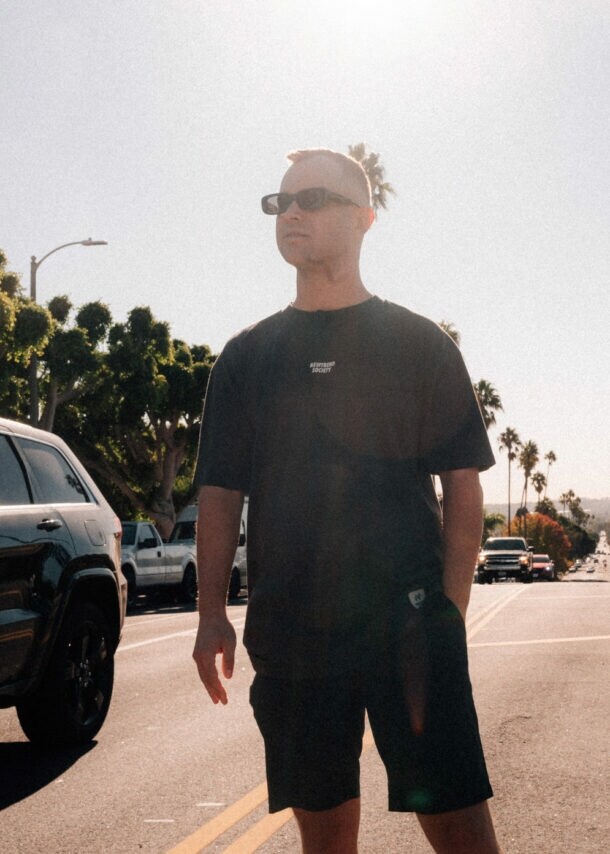 Benjamin Diedering posiert mit Sonnenbrille auf einer palmengesäumten Straße bei Sonnenschein.