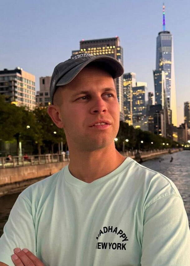 Porträt von Benjamin Diedering mit Baseballcap vor der Skyline New Yorks am Wasser.
