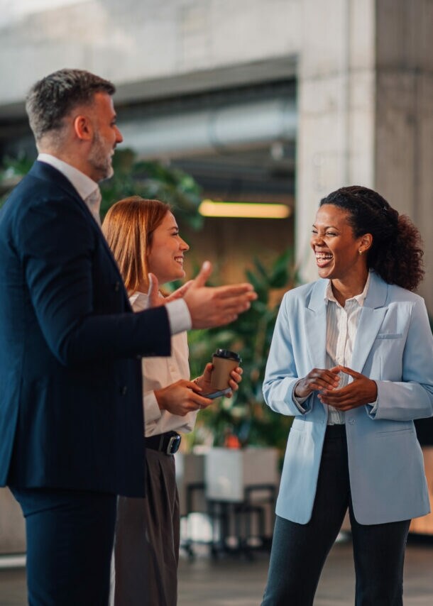 Zwei Frauen und zwei Männer in Business-Kleidung stehen beieinander und kommunizieren lächelnd in einem Foyer.
