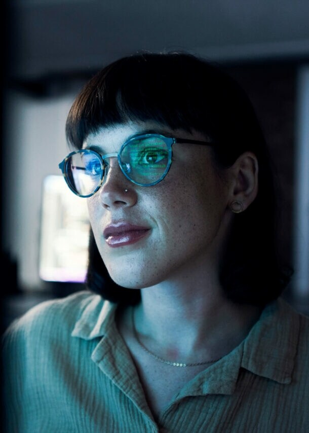 Eine Frau mit einer Brille in einem dunklen Raum vor einem Bildschirm.