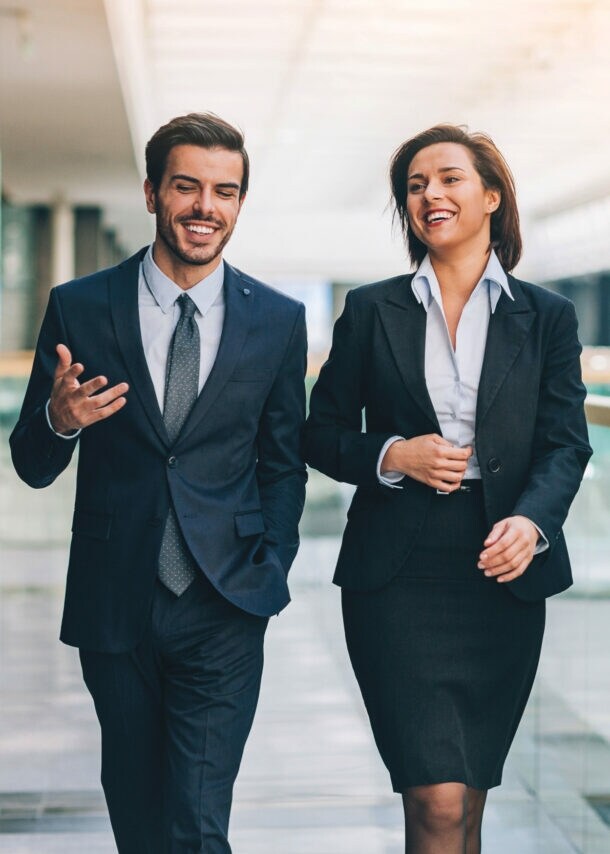 Ein Mann und eine Frau in formeller Business-Kleidung kommunizieren nebeneinander gehend.