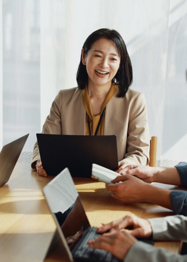 Eine Gruppe asiatischer Menschen sitzt lächelnd mit Laptops an einem Tisch.
