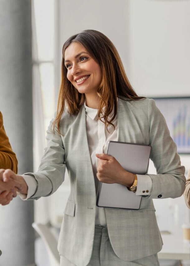 Vier Personen stehen beieinander, zwei Frauen geben sich lächelnd die Hand, während zwei Männer in die Hände klatschen.