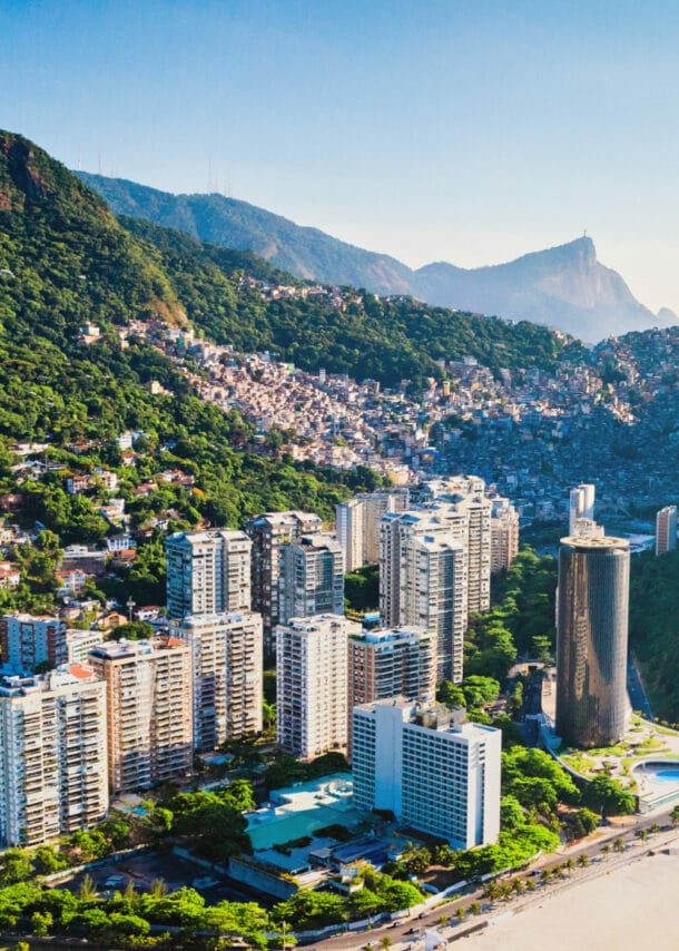 An einem Strand liegt eine Stadt mit Hochhäusern und riesigen Bergen.