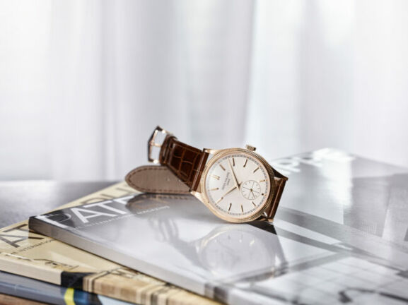 Eine klassische Herrenuhr von Patek Philippe mit braunem Lederarmband, goldener Lünette und hellem Zifferblatt auf Hochglanzmagazinen