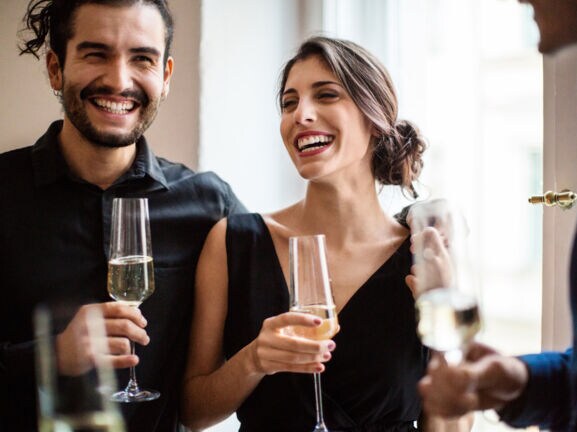Ein fröhliches Paar in festlichen Outfits mit einem Glas Champagner in den Händen.