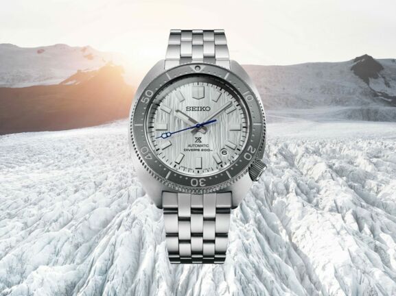 Uhr mit silbernem Armband und Ziffernblatt vor einer weißen, bergigen Schneelandschaft