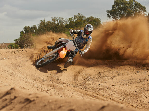 Eine Person fährt auf einem Motocrossbike um die Kurve und wirbelt Sand auf