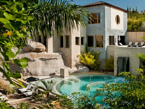 Resort des Bahia del Duque auf Teneriffa mit Poolanlage, Begrünung, Holzterrasse und Liegen.