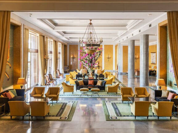 Ein elegantes Hotelfoyer mit Marmorsäulen und gelben Sesseln, in der Mitte ein großes Blumenbouquet.