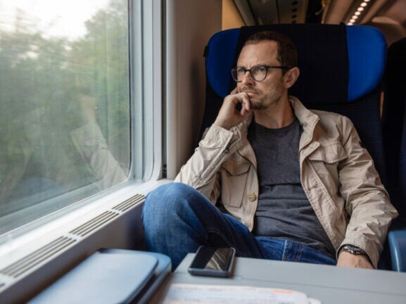 Mann sitzt in fahrendem Zug und schaut aus dem Fenster.