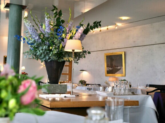 Innenraum des Restaurants Wielandshöhe mit einem Holztisch, weiß eingedeckten Tischen und Blumendeko.