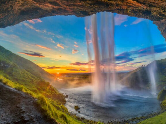Wasserfall, der von einer Höhle aus bei Sonnenuntergang in eine grüne Landschaft fällt