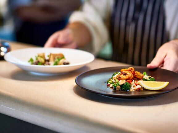 Ein Koch stellt zwei Teller mit zubereiteten Speisen auf die Theke.