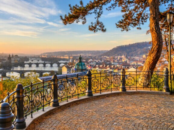 Blick auf die Moldau mit mehreren Brücken und der Altstadt von Prag im Sonnenuntergang, von einer Aussichtsplattform mit schmiedeeisernem Geländer