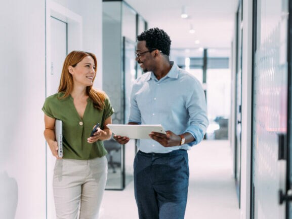 Eine Frau und ein Mann mit Tablets in den Händen kommunizieren auf einem hellen Flur.