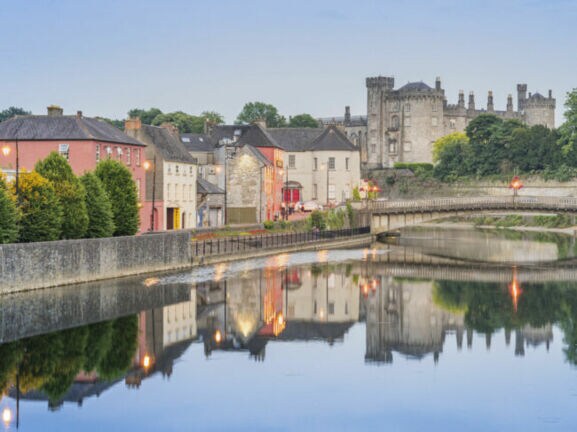 Blick auf Kilkenny mit Kilkenny Castle und der John’s Bridge vor dem Fluss Nore, indem sich die Lichter und Gebäude siegeln.