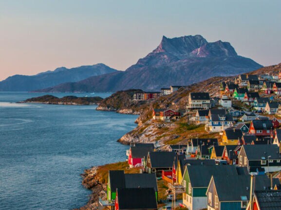 Bunte Häuser der grönländischen Hauptstadt Nuuk an einem Hang, der zum Wasser hin abfällt, im Hintergrund sind Berge.