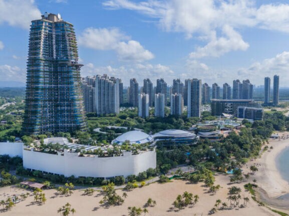 Blick auf eine moderne Küstenstadt in Ägypten mit hohem, runder Turm im Bau, mehreren Hochhäusern und einem Sandstrand am Meer.