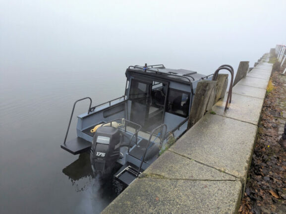 Ein Motorboot liegt bei dichtem Nebel an einer Kaimauer.