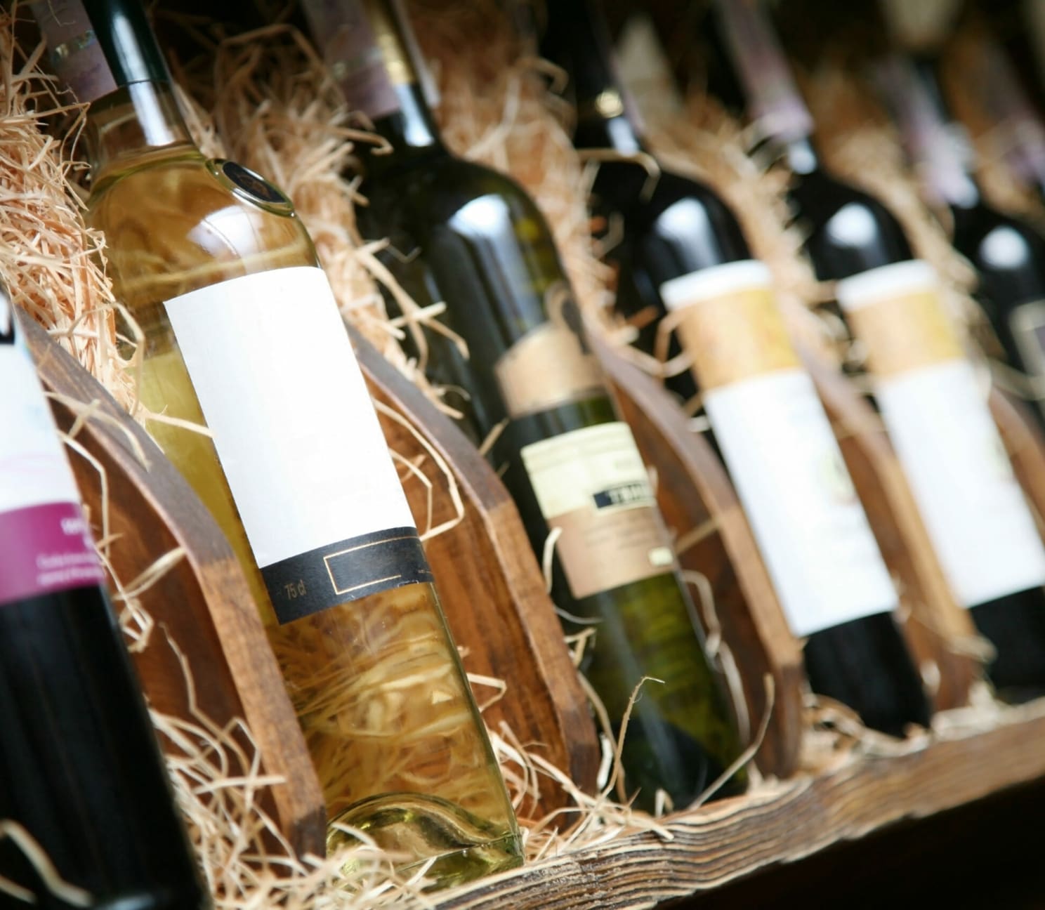 Mehrere Weinflaschen aufgereiht in einer Holzkiste, auf Stroh gebettet.