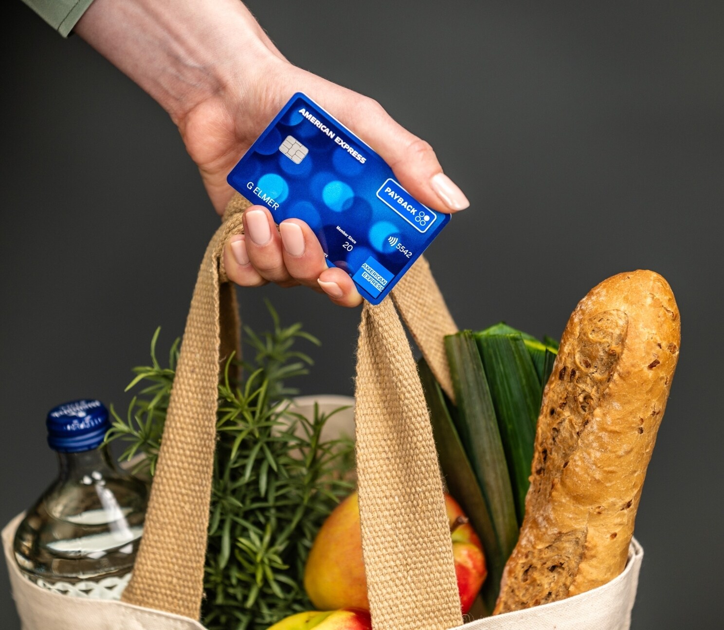 Eine Person hält eine volle Einkaufstasche und ihre PAYBACK Amex Karte in der Hand.