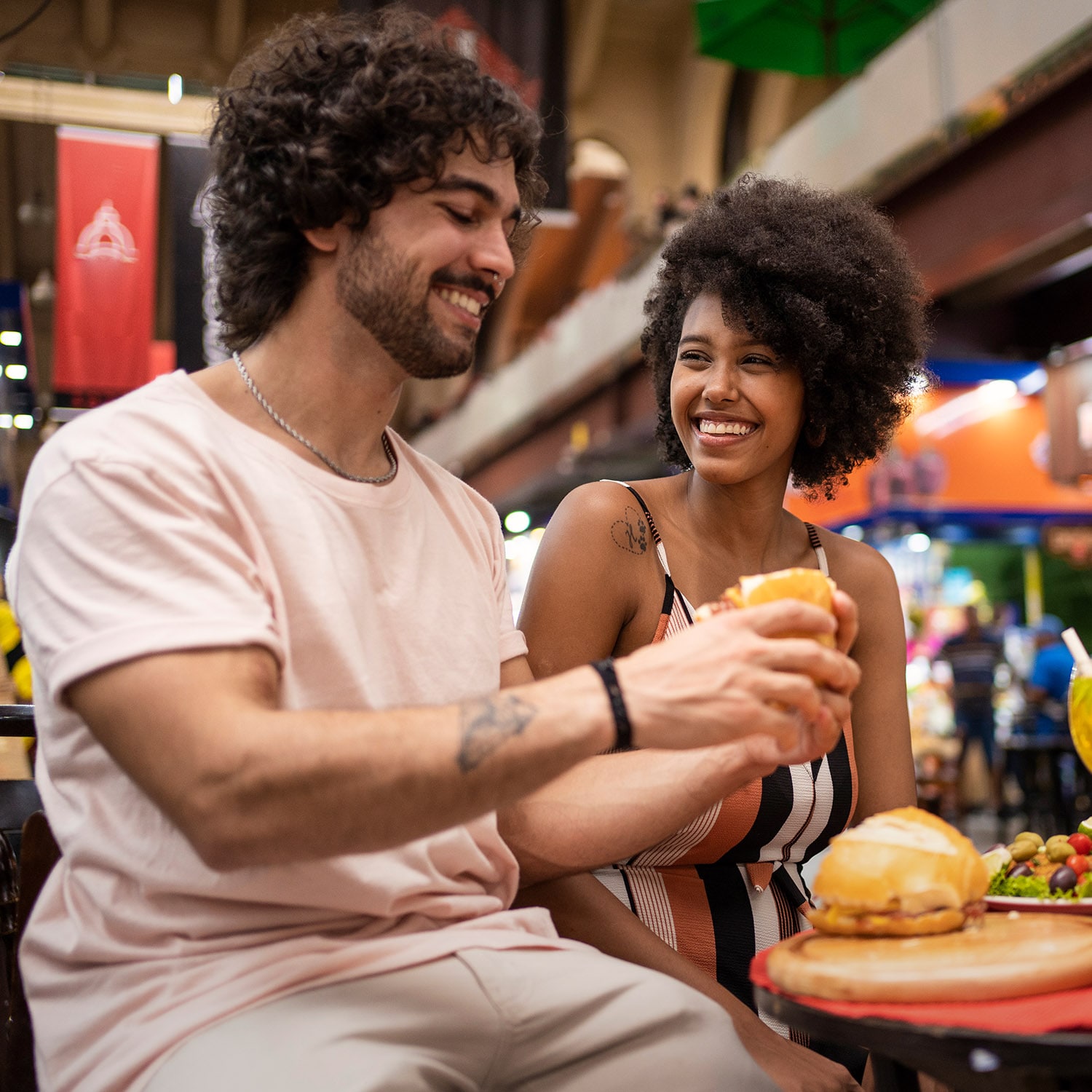 Ein modernes, fröhliches Paar beim Essen in einer Markthalle.