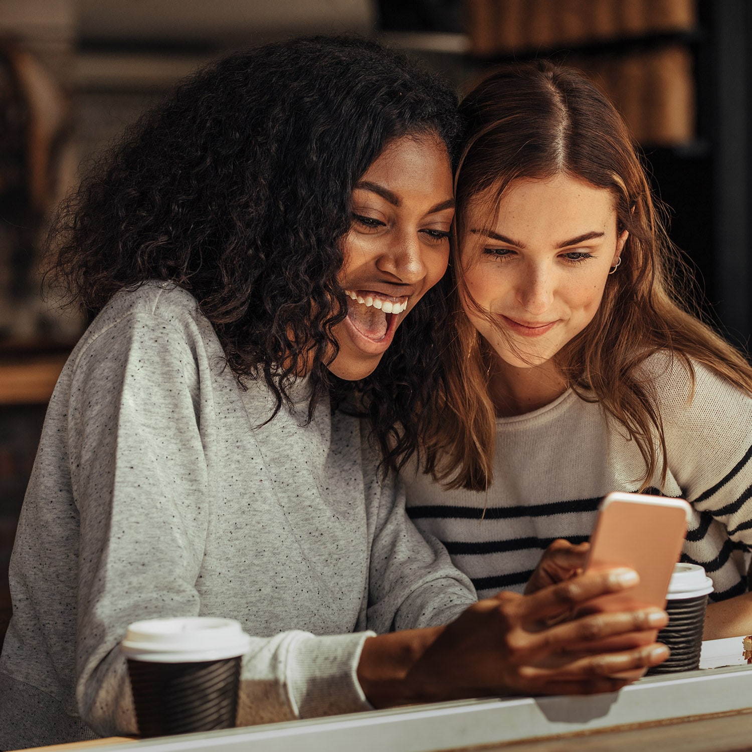 Zwei Freundinnen schauen gut gelaunt gemeinsam auf ein Smartphone in einem Café.