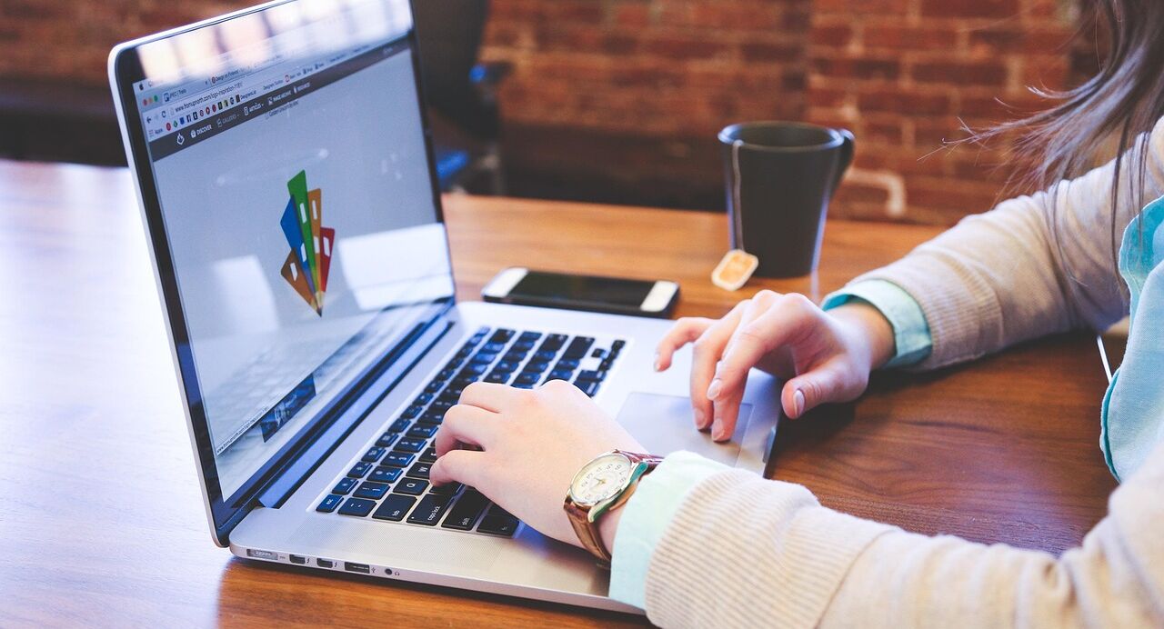 Person arbeitet an einem Laptop in einem modernen Büro mit Notizblock, Smartphone und Teetasse auf dem Schreibtisch