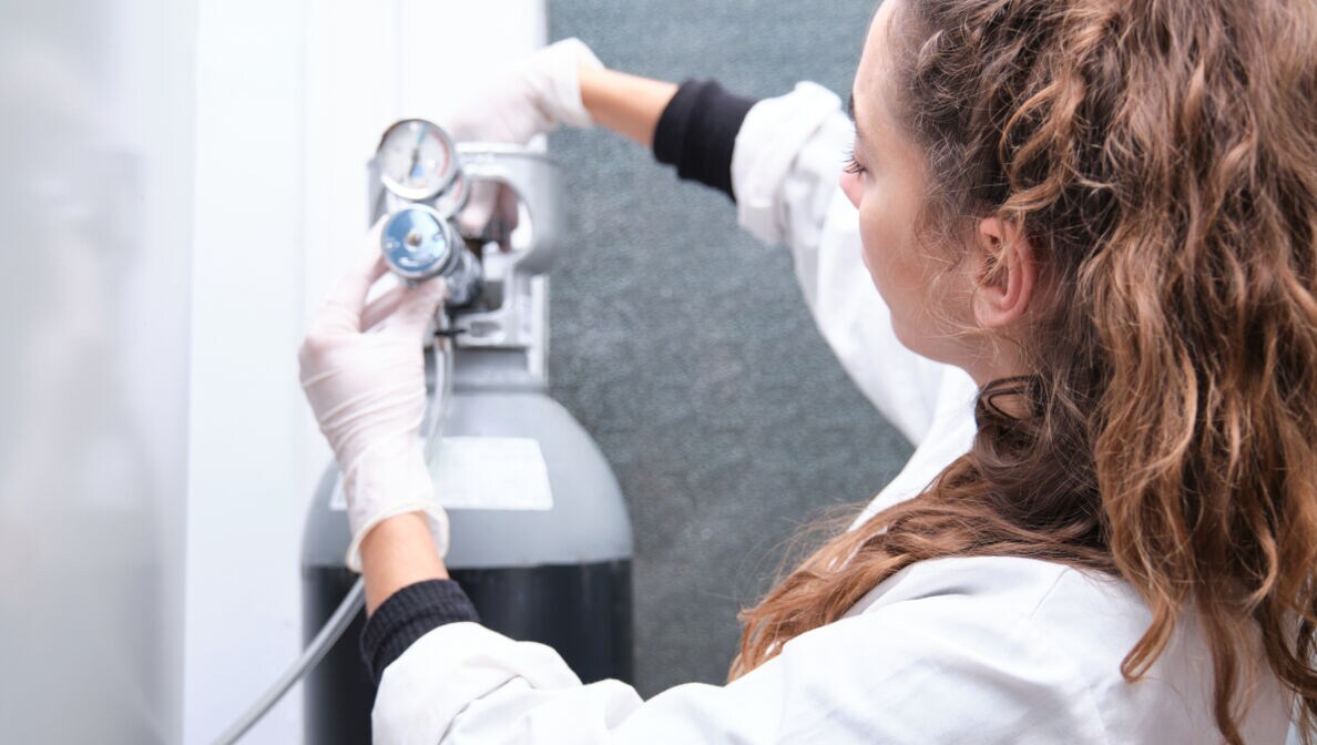 Eine Frau im weißen Kittel schraubt an einer Gasflasche