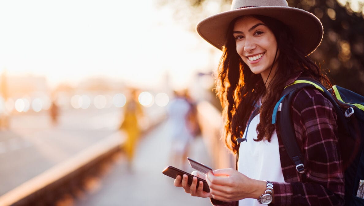 Eine lachende junge Frau mit Smartphone und Kreditkarte in der Hand