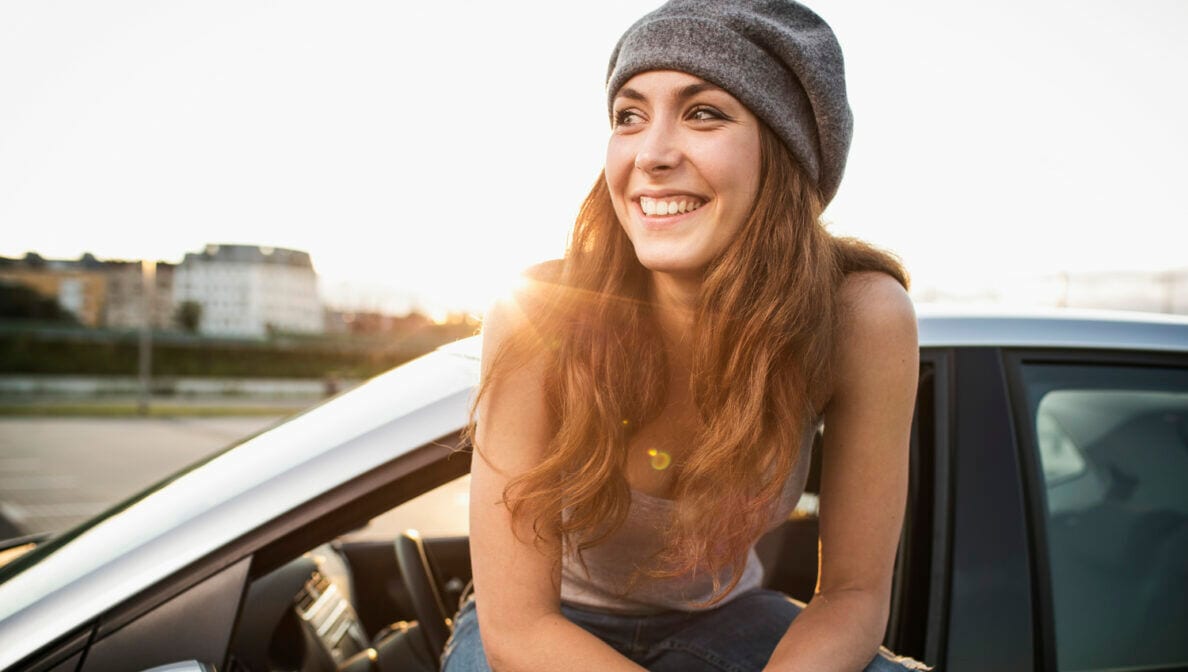 Eine junge Frau sitzt lächelnd vor einem Auto
