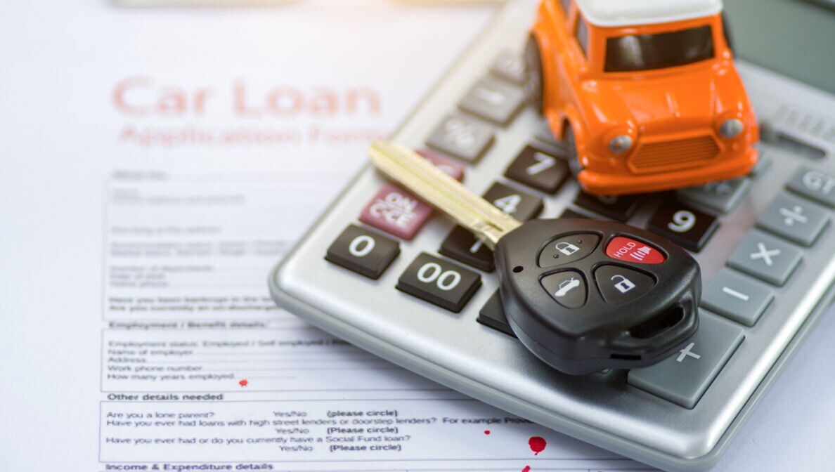 Auf den Papieren für einen Autokredit liegen ein Taschenrechner, ein Autoschlüssel und ein Spielzeugauto.