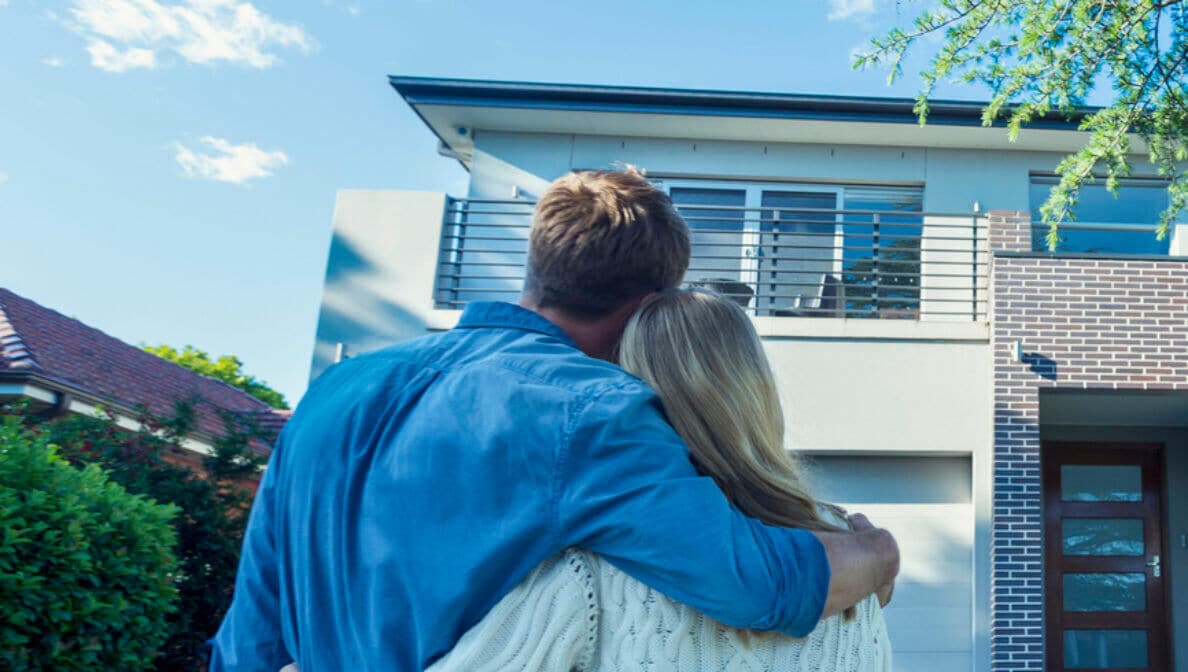 Rückenansicht einer Paares, das Arm in Arm auf ein neues Haus blickt