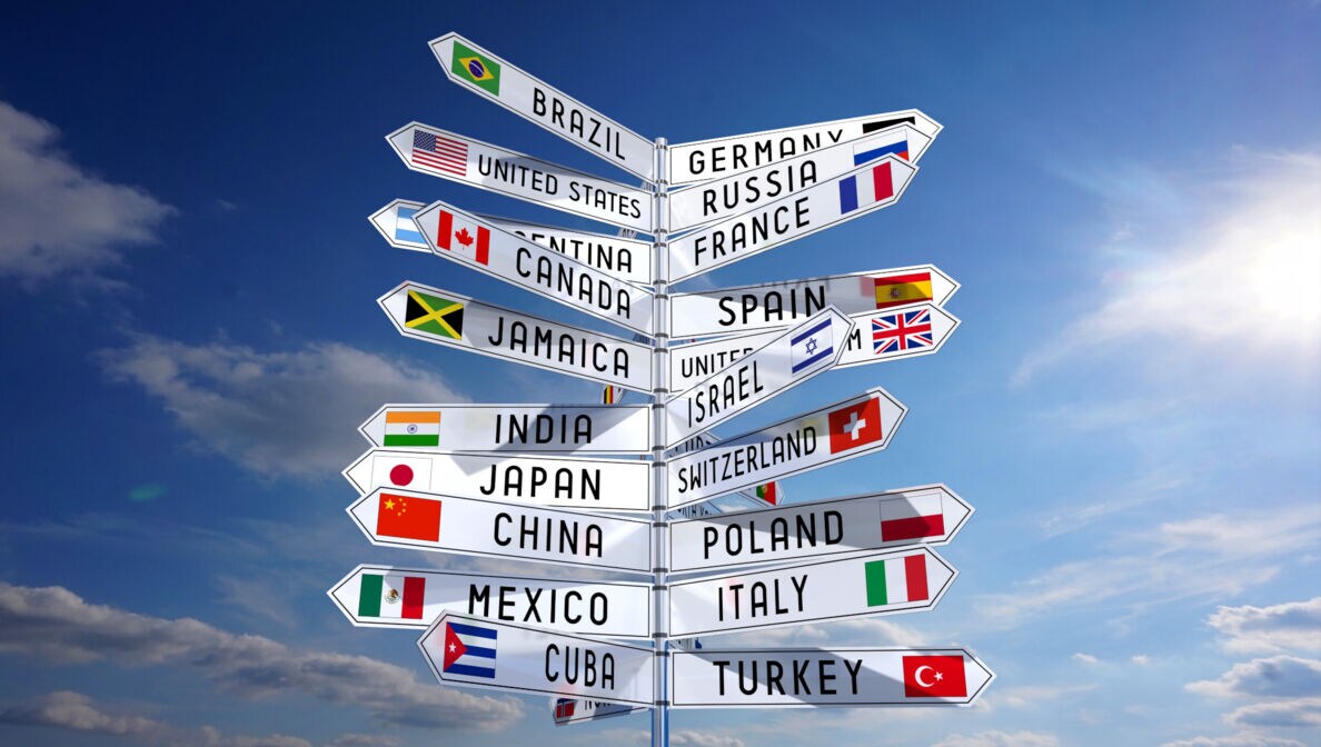 Wegweiser mit Nationalflaggen verschiedener Länder vor blauem Wolkenhimmel