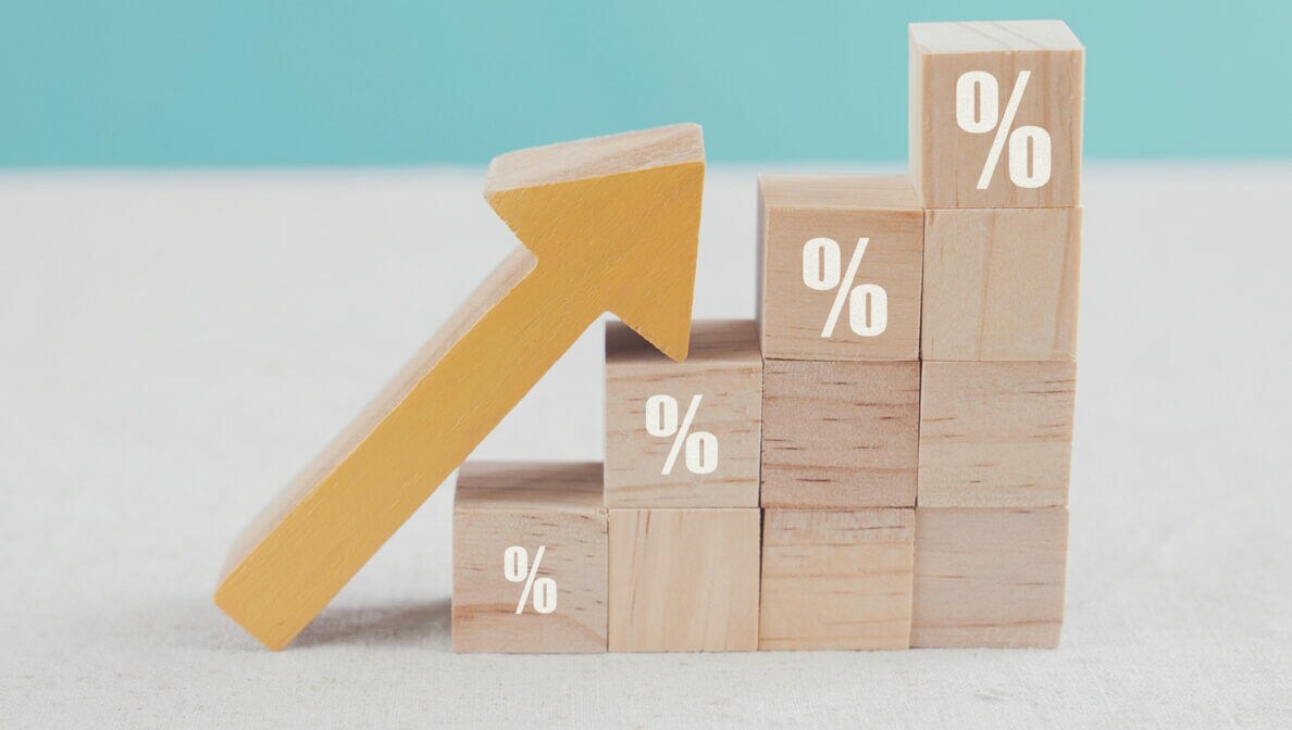 An treppenförmig aufgebauten Bauklötzen mit aufgedruckten Zinszeichen lehnt ein nach oben zeigender Pfeil