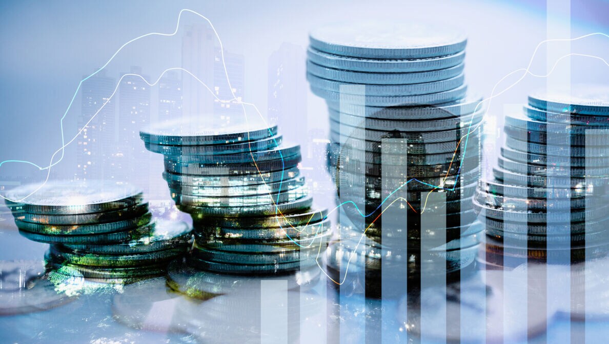 Mehrere Geldmünzenstapel nebeneinander, darüber verlaufen Aktienkurse und Säulendiagramme.