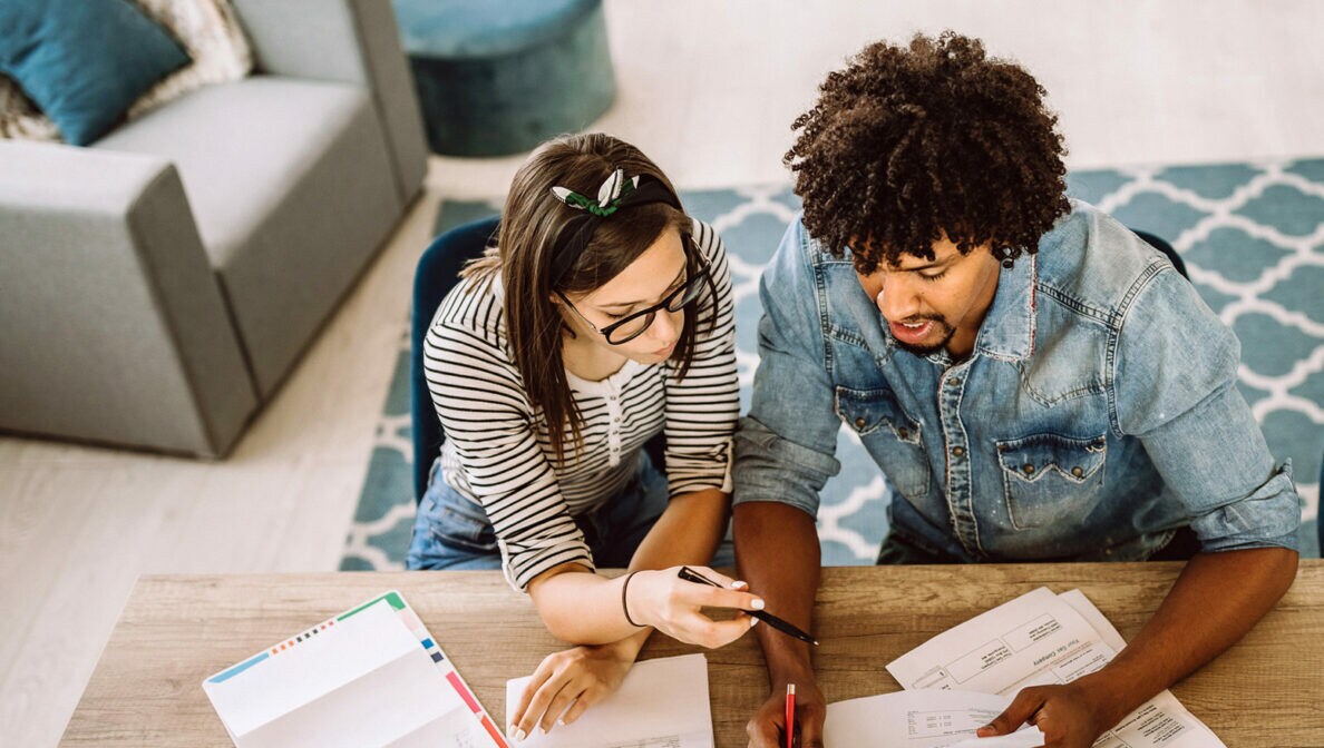 Ein Paar sitzt an einem Tisch und wälzt diverse Dokumente.